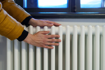 Cropped photo of woman warming hands near radiator at home after walking in cold winter weather,...