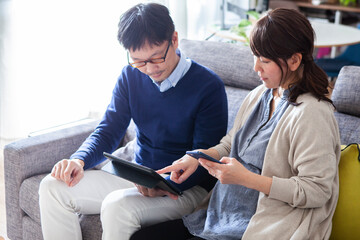 スマートフォンとデジタルタブレットの操作をする妊娠している夫婦