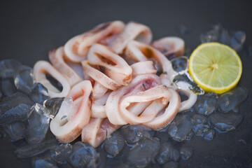 squid rings on ice, Fresh raw squid with salad seafood lemon on black plate background