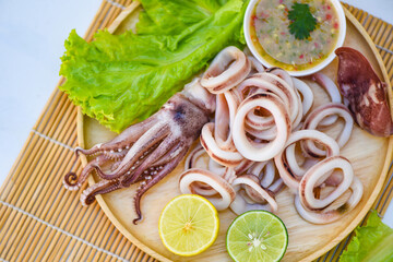 squid rings on wooden plate, Fresh squid cooked boiled with lettuce vegetable salad lemon and seafood sauce on table background