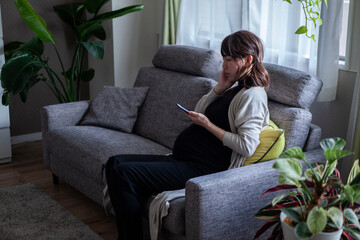 スマートフォンを眺める不安な様子の妊婦女性