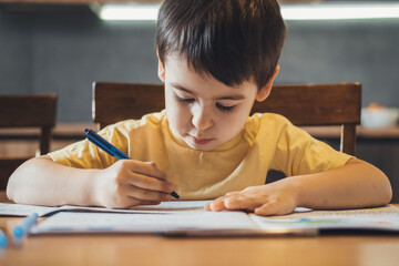 Caucasian boy studying at home writing notes sitting at desk. Front view. Distance education. Front...