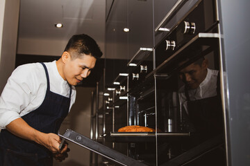 The joy of making homemade : Handsome chef refined with home-made breads and a modern oven : Happy and smiling Asian man prepares freshly cooked bread in the oven.