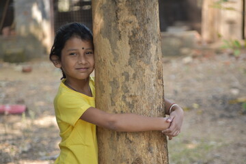 A girl kid holding tree trunk with her arm happy expressions selectively focused blur background