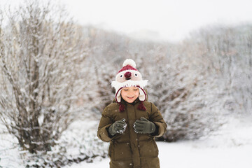 Child enjoying winter. Cute little boy in funny winter hat walks during a snowfall. Outdoors winter activities for kids. Winter Christmas and lifestyle concept.
