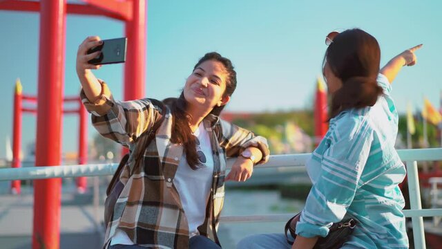 Young sister taking selfie picture using smart phone app on cellphone for social media. Concept of holiday with friend at river by boat with city traveling, best friend travel lifestyle.