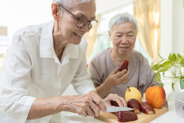 Fototapeta na wymiar Happy asian senior grandmother cutting the fresh fruit into slices with a knife,healthy elderly people enjoy tasting delicious fruits,preparing healthy meal,cooking,healthy food,health care concept
