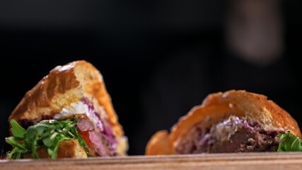 Cut craft burger is cooking on black background. Consist: sauce, lettuce, tomato, red onion,...