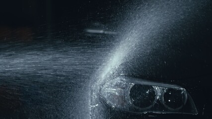 Car headlight wash. Washing modern vehicle body by high pressure jet wash hose water. Auto glass headlamp, angel eyes in drops.