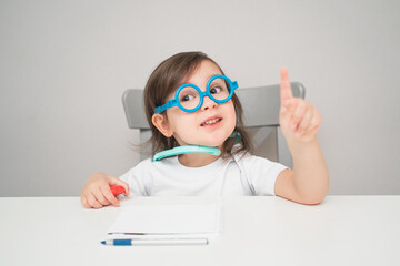 A small child in a doctor's costume. An artistic girl plays doctor. A child in glasses and a white T-shirt.