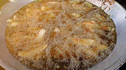 Golden brown deep-fried sliced bananas in hot oil pan, Thai snack street food.