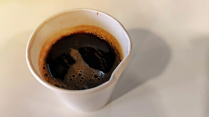 A hot black coffee in white paper cup on white wooden table.