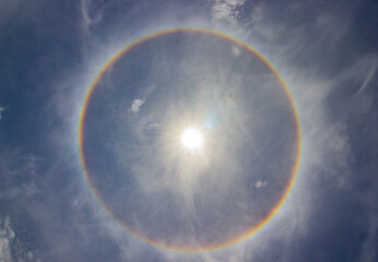 circular rainbow halo around the sun among blue sky and white clouds. - Powered by Adobe