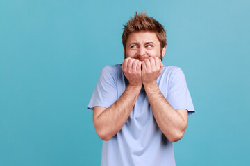 Anxiety disorder. Portrait of stressed out, worried bearded man biting nails, nervous about troubles, panicking and looking scared. Indoor studio shot isolated on blue background. - obrazy, fototapety, plakaty