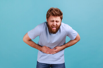 Portrait of unhealthy bearded man standing and holding his painful belly, feeling bad, suffering...