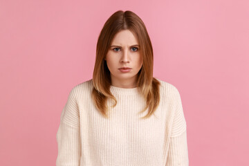 Fototapeta premium Portrait of young adult angry serious blond woman looking at camera with strict negative expression, aggression, wearing white sweater. Indoor studio shot isolated on pink background.