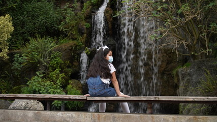 Young Girl With Surgical Mask Sitting In Front of Waterfall