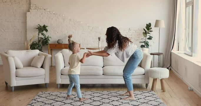 Latina mother dancing with little daughter in living room, full-length. Happy woman hold whirling her cute preschool girl, carefree family enjoy music spend active leisure indoor. Fun, hobby concept