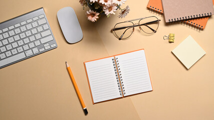 Top view notebook, glasses, keyboard and flower pot on beige background.