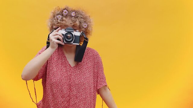 Happy young girl taking a picture with a vintage camera. Photography Concept. Yellow background studio
