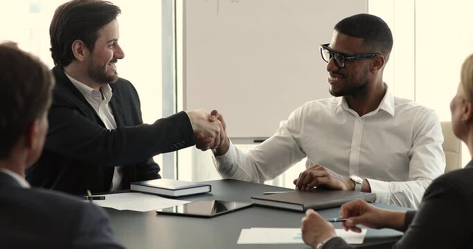 Accomplish successful negotiations, make profitable deal concept. Multi ethnic business partners succeed goal, finish appointment in office board room shake hands feeling satisfied by meeting result