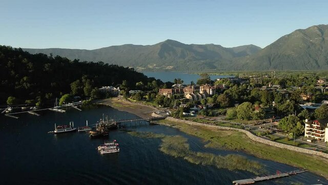 Aerial orbit of the main dock of pucon with ships with the chilean flag and the background of mountains and its main beach at sunset - drone shot