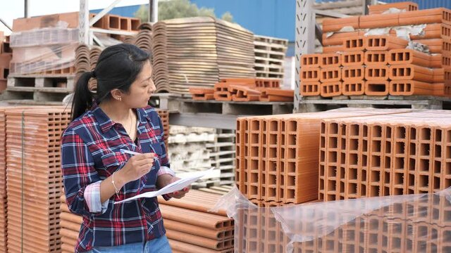  Concentrated hispanic woman worker controlling quantity of bricks at hardware store warehouse