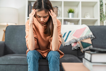 Obraz premium Tired young Asian woman sitting on sofa and have a headache because migraine.