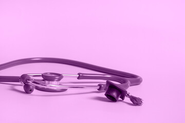 Fototapeta premium Graduation cap with stethoscope and numbers 2022 on violet background, closeup with copy space. Medical education concept.