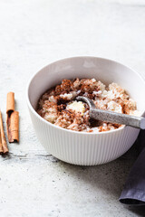 Scandinavian rice porridge with cinnamon and butter in white bowl on gray background. Norwegian cuisine concept.