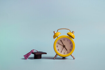 Yellow alarm clock with graduation cap on blue background closeup with copy space