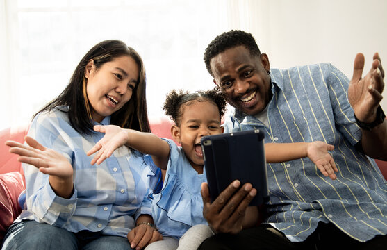 Diverst family using a tablet to take family photos with mixed race daughter on sofa in the living room. Warmth and brightness of the crowd