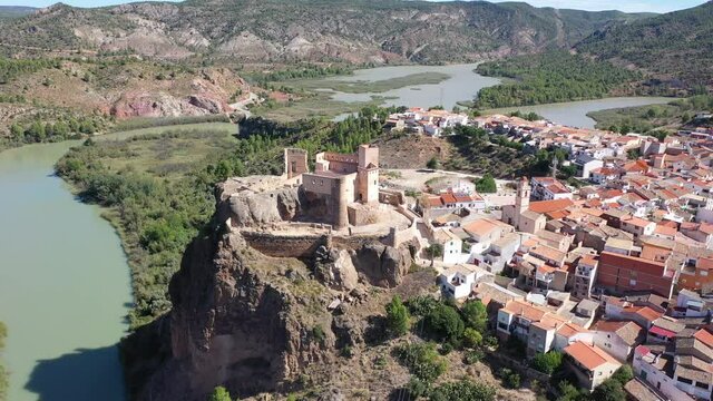 Scenic aerial view of medieval Cofrentes Castle towering over city residential buildings atop rocky cliff over Cabriel River, Valencia, Spain. High quality 4k footage