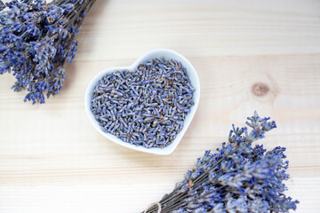 Dried lavender flowers in a heart-shaped bowl on a wooden background. Flat lay, place for text.