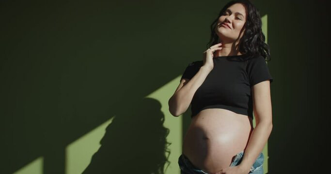 A pregnant woman feels happy with her new life at home, taking care of her baby. A young pregnant mother holds a baby in the belly of a pregnant woman. Pregnancy care and woman pregnancy concept.