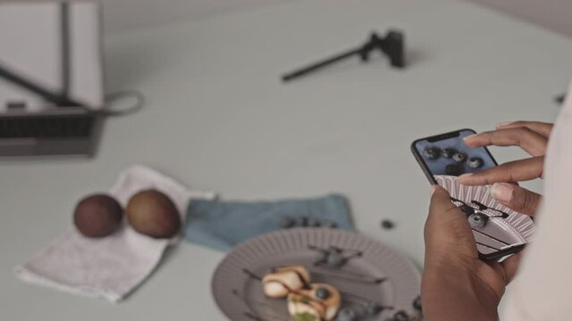 Medium closeup of unrecognizable African-American woman taking pictures of delicious blueberry cheese pancakes on smartphone