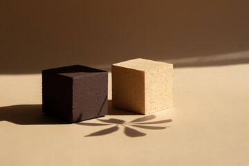 Two square stands made of polystyrene, brown and beige, in rays of sunlight and shadow of palm...
