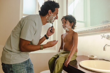 Cheerful father showing his son how to shave at home