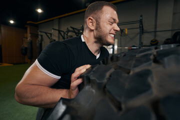 Naklejka premium Strong energetic Caucasian sportsman performing tire exercise