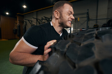 Strong energetic Caucasian sportsman performing tire exercise