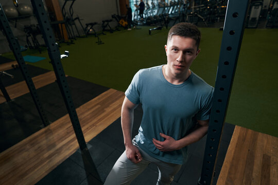 Tranquil sportsman posing for camera among gym equipment