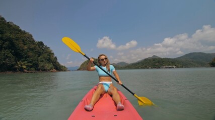 Sportive woman rows pink plastic canoe along sea water.