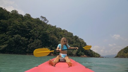 Sportive woman rows pink plastic canoe along sea water. Positive sports girl hand padding on kayak, front view.