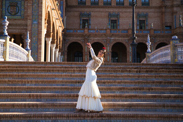 Obraz premium Flamenco dancer, woman, brunette and beautiful typical spanish dancer is dancing and clapping her hands on the stairs of a square in seville. Flamenco concept of cultural heritage of humanity.