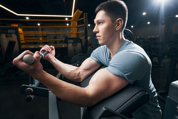 Concentrated bodybuilder doing upper-body exercise on fitness equipment