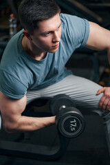 Fototapeta na wymiar Concentrated sportsman lifting one dumbbell from seated position