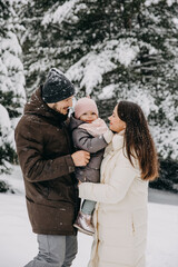 Mother and father holding little girl in arms outdoors on a snowy winter day in mountains.