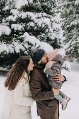 Mother and father holding in arms little daughter, outdoors, on a snowy winter day, warming up her nose.