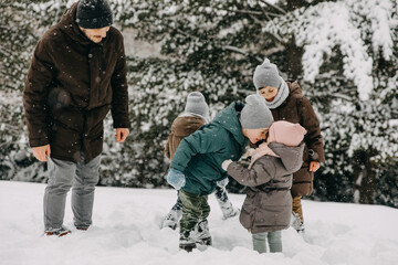 Family spending time outdoors on snowy winter day in a forest, playing in snow.