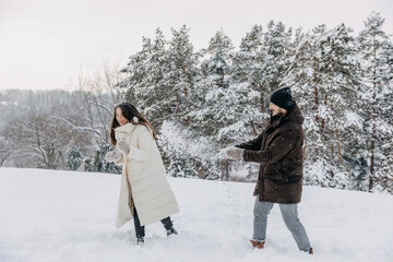 Fototapeta na wymiar Happy couple spending fun time outdoors, playing with snowballs on a cold winter day.